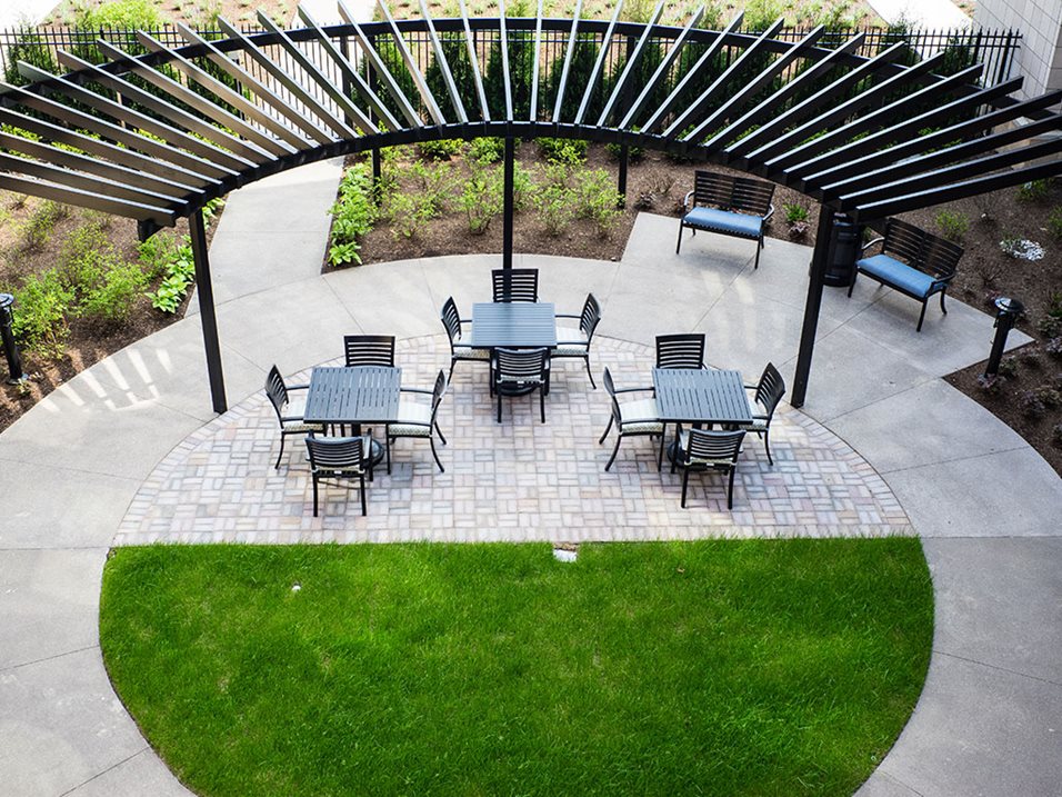 An aerial view of an outdoor patio with tables, chairs, benches, and a black pergola structure.