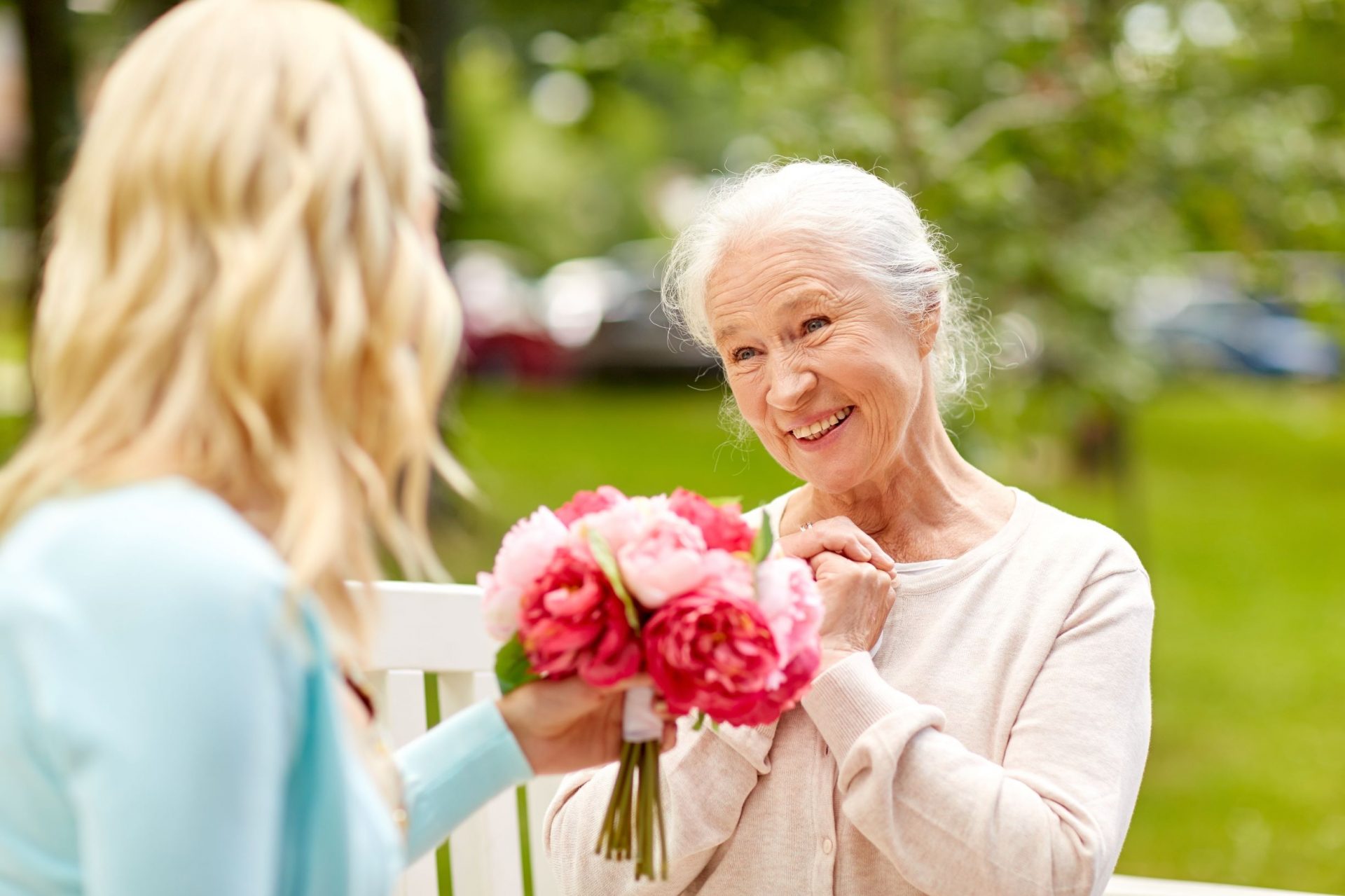 Elderly woman sitting on a bench, gratefully receiving a bouquet from a younger woman.