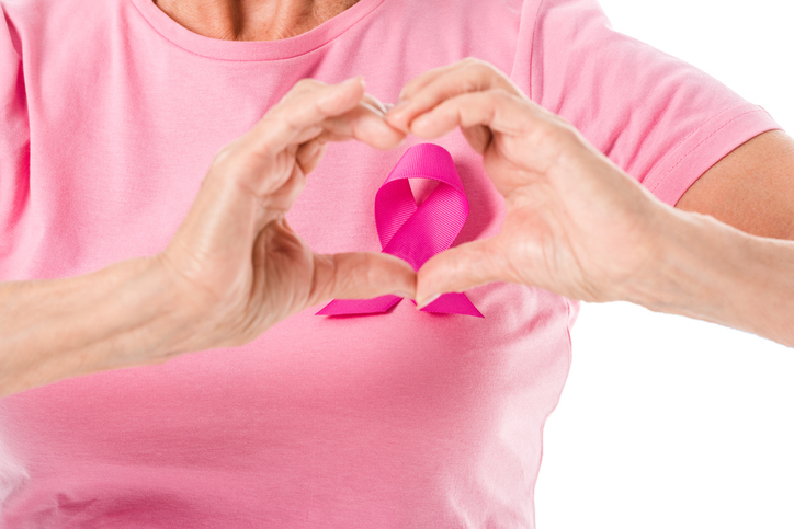 A person wearing a pink shirt with a pink ribbon, forming a heart shape with their hands